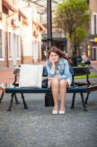 sad woman sitting on bench with shopping paper bag