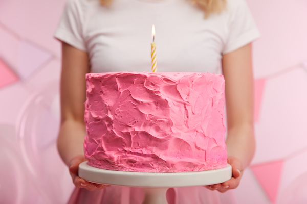 woman holding pink birthday cake | do I need to bring a birthday gift?